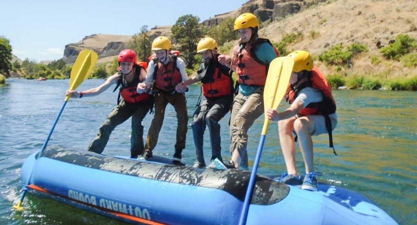 a group of outward bound students stand on the underside of a raft during a rafting exercise 
